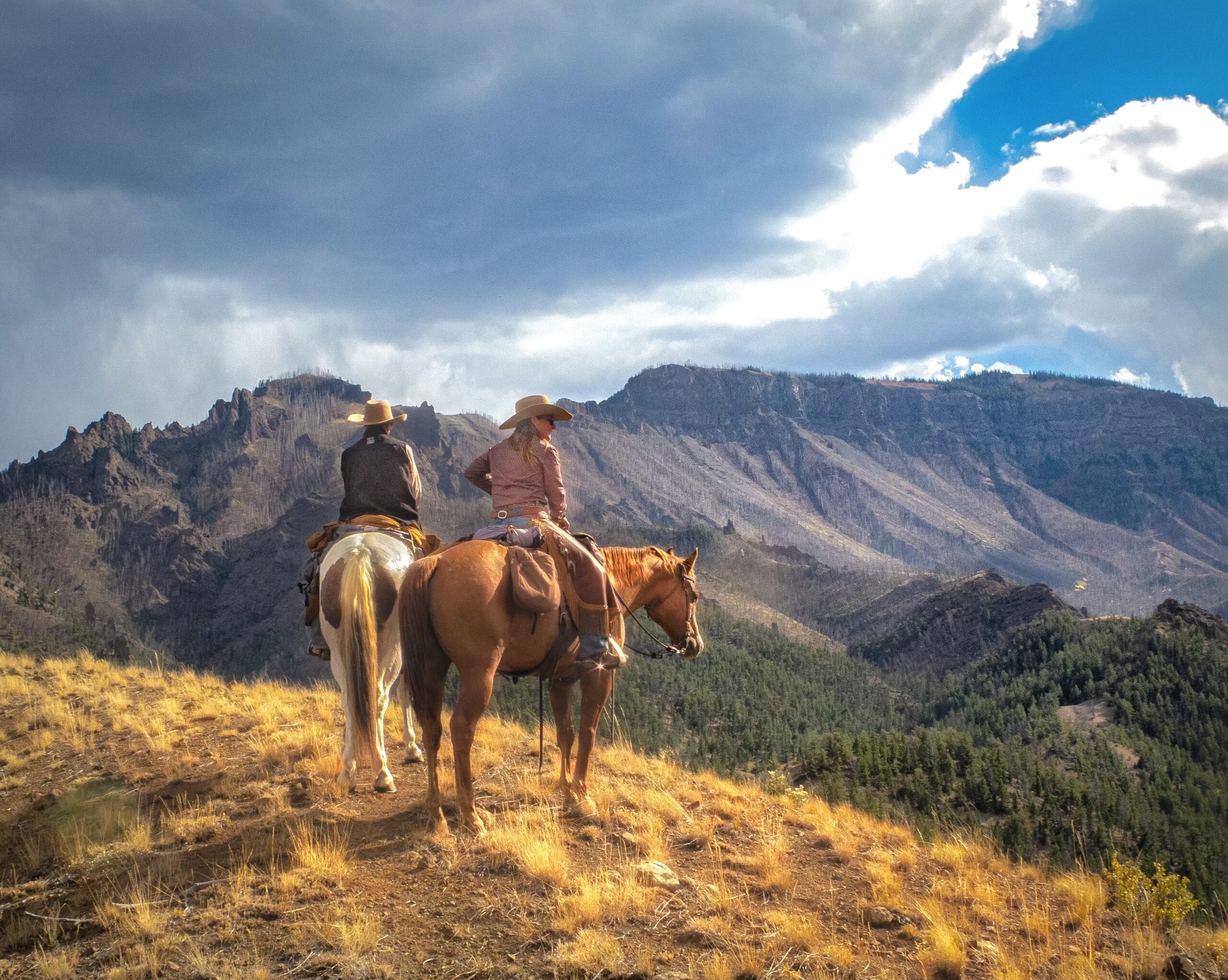 Last ride photo - two horsemen riding on horseback over looking the mountain range near UXU Ranch